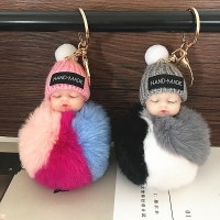Sleeping baby doll keychain with faux rabbit fur pom pom, cute and plush bag charm for women.
